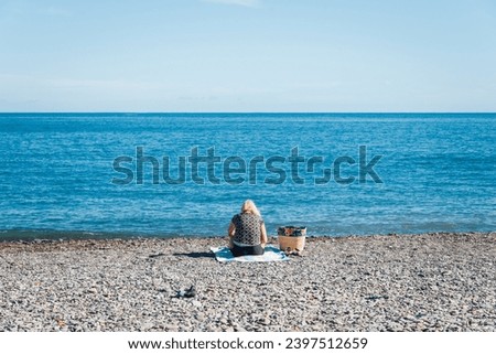 a woman sitting alone on the beach facing the sea. A person with her back on the Mediterranean beach. Woman facing the horizon. Holidays at the sea. Alone on the beach. Relax by the sea. Relaxation. 