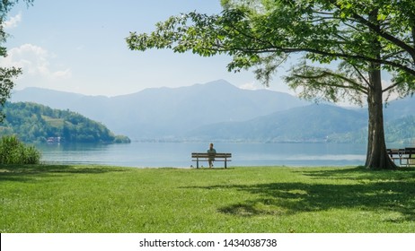 Woman sitting alone on a bench. Attractive girl sits on a wooden bench with amazing view over lake and mountains.Female enjoing a picturesque place. Recreation,peace,mindfulness and relaxation concept