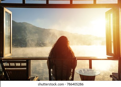 A woman sitting alone in a room among fog and looks outside opened window seeing mountain and sunrise in a cold winter day. - Powered by Shutterstock