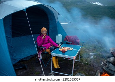 Woman, Sitting Around Campfire At Night, Enjoying Wild Camping, Family Vacation In Norway Summertime