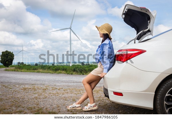 Woman sitting at the back of a car\
resting on vacation with wind turbines and sky\
background