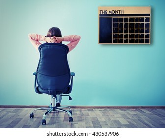 Woman Sitting Back On The Office Chair And Looking At Chalkboard Calendar On Wall Background