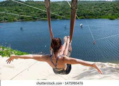 Woman Sitting Back To Back On A Zip Line Overlooking Jacomã Lagoon In The City Of Cerá Mirim-RN / Brazil.