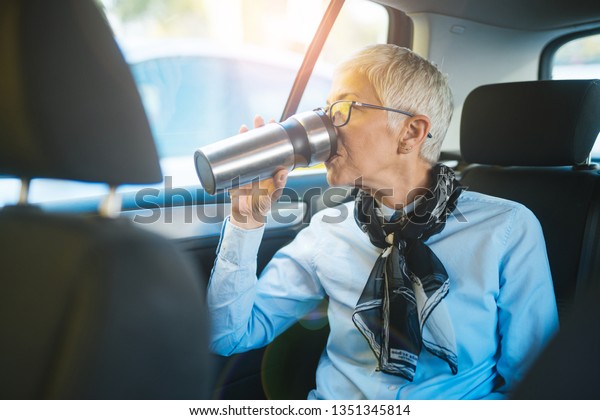 Woman sitting in the back seat of the car and\
drinking coffee