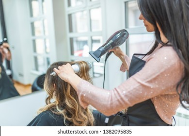 Woman sitting at beauty salon, making hairdo. Beautician drying woman's hair. Young woman talking with her hairstylist during a salon appointment