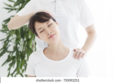 A woman sitting in bed and receiving shoulder and neck massage.