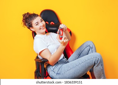 Woman Sitting Behind Gaming Chair In Her Hands Holding Red Gamepad On Yellow Background.