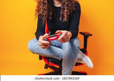 Woman Sitting Behind Gaming Chair In Her Hands Holding Red Gamepad On Yellow Background.