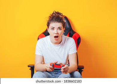 Woman Sitting Behind Gaming Chair In Her Hands Holding Red Gamepad On Yellow Background.