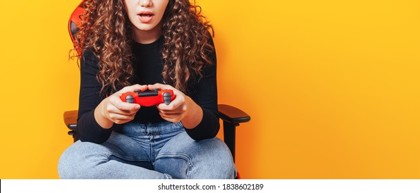 Woman Sitting Behind Gaming Chair In Her Hands Holding Red Gamepad On Yellow Background.