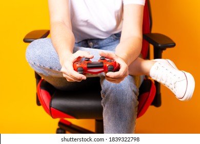 Woman Sitting Behind Gaming Chair In Her Hands Holding Red Gamepad On Yellow Background.