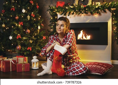 Woman sitting beside fireplace and searching gifts in Christmas stocking - Powered by Shutterstock