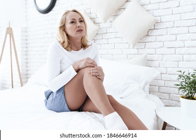 A Woman Is Sitting With A Bruised Knee And A Sad Face On The Bed. Woman Does Knee Massage And Feels Sharp Pain. 