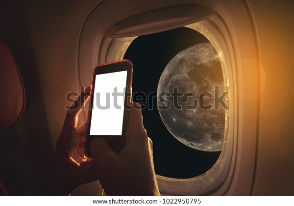 Woman sitting by aircraft window and using a\
digital mobile during the flight. The moon as seen through window\
of an aircraft.