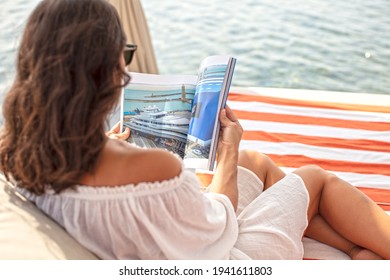 Woman Sitting At  Cabana And Reading Marine  Magazine At Beach