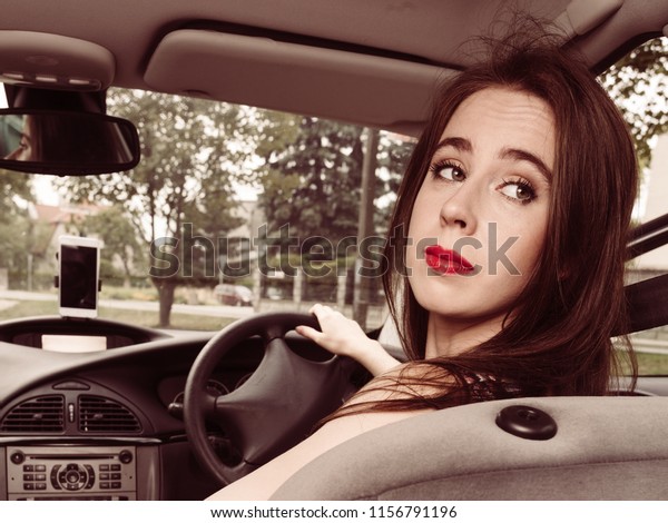 Woman\
sitting in car behind steering wheel riding transport vehicle\
looking behind during parking or driving\
backwards