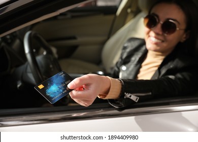 Woman sitting in car and giving credit card at gas station, focus on hand
