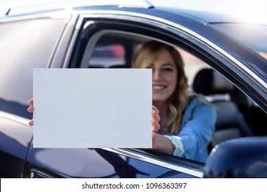 Woman sitting in the car and holding a white blank poster. Attractive blonde with a clean sheet of paper or your text. - Powered by Shutterstock