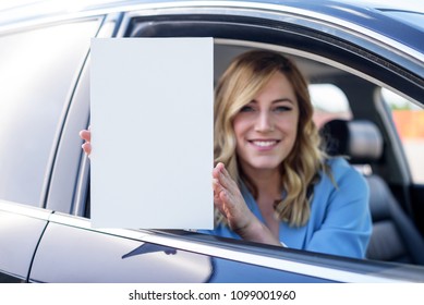 Woman sitting in the car and holding a white blank poster. Attractive blonde with a clean sheet of paper or your text. Focus on paper. - Powered by Shutterstock