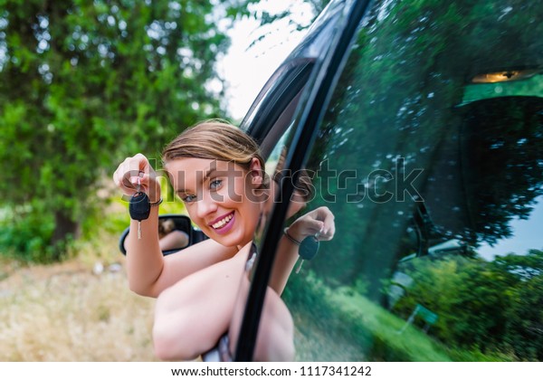 Woman Sitting In Car With Key. Happy woman with\
key. Woman buying car. Woman Driver Holding Keys siting in Her New\
Car. Driving towards the\
fun
