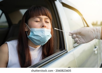 Woman sitting in car for medical worker through car window to perform drive-thru COVID19 test. Doctor or healthcare hand white glove with cotton swab making coronavirus test for young lady in her car.