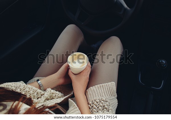 Woman sitting\
in a car with a paper coffee cup.\
