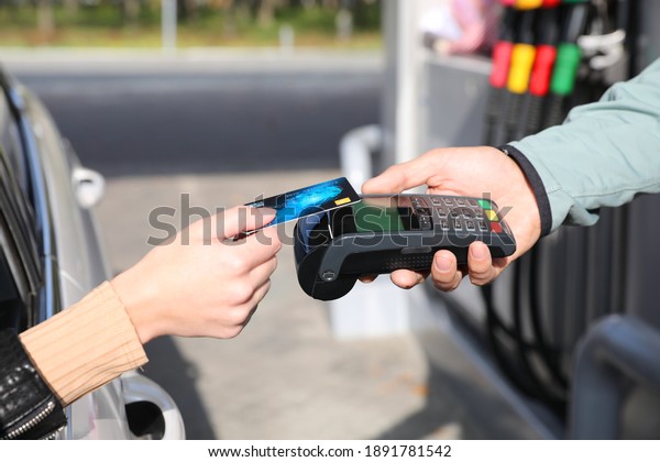 Woman sitting in car and paying with credit card\
at gas station, closeup