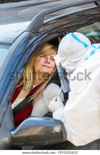 Woman sitting in car, waiting for medical worker to\
perform drive-thru COVID-19 test, taking nasal swab sample through\
car window, PCR diagnostic for Coronavirus, doctor in PPE holding\
test kit.