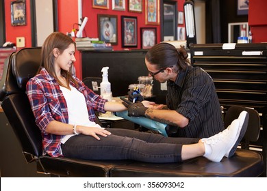 Woman Sitting In Chair Having Tattoo On Arm In Parlor