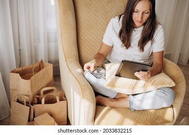 Woman sitting in a chair, holding credit bank card and using tablet for online shopping at home. Selective focus