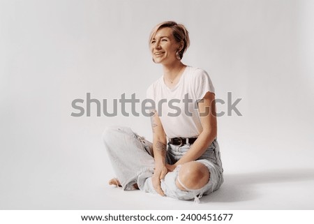 Woman sitting cross-legged, laughing in light denim jeans and a white t-shirt, embodying a carefree spirit