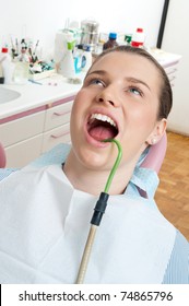 Woman Sitting In Dentist Chair With Suction Tube In Her Mouth