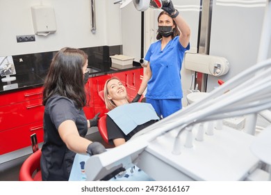 A woman is sitting in a dentist's chair with two women standing behind her. - Powered by Shutterstock