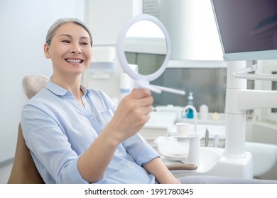 Woman sitting at the dentists office with a mirror in hands - Shutterstock ID 1991780345