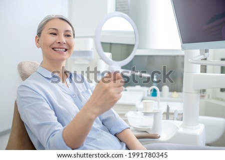 Woman sitting at the dentists office with a mirror in hands