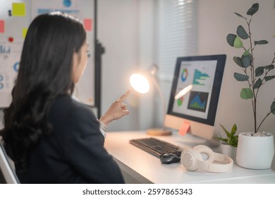 Uma mulher está sentada em uma mesa com um monitor de computador na sua frente. Ela está apontando para a tela com o dedo. Conceito de foco e concentração enquanto a mulher trabalha em seu computador
