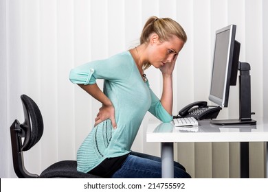 A Woman Sitting At A Desk And Has Pain In The Back. Symbol Photo For Proper Posture At Work In The Office.