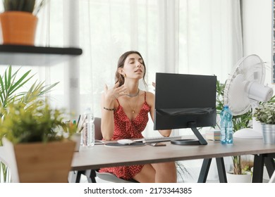 Woman sitting at desk at home during a summer heat wave, she is cooling herself with an electric fan - Powered by Shutterstock