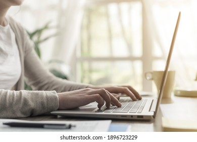 Frau sitzt zu Hause am Schreibtisch und arbeitet mit ihrem Laptop, sie tippt auf die Tastatur