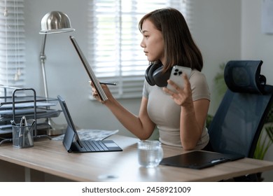 A woman is sitting at a desk with a laptop and a cell phone. She is wearing headphones and she is focused on her work