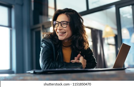 Woman sitting at the desk with laptop looking away and smiling. Asian woman in casuals at office.