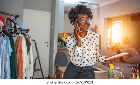 Woman Sitting At Desk And Making A Phone Call. Businesswoman Working From Home Office And Using Cell Phone. Beautiful Afro American Woman Sitting At The Desk In A Home Office And Using A Smart Phone.