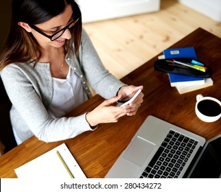 Woman sitting at desk working, smiling and looking at mobile phone.