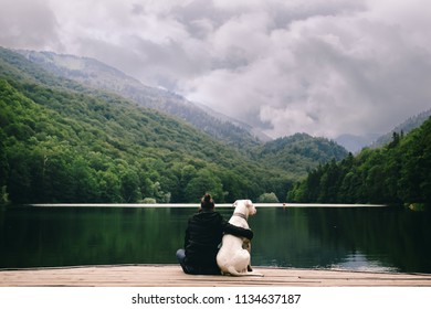 Woman Sitting With A Dog On Dock At The Lake