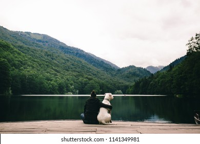 Woman Sitting With A Dog On Dock At The Lake