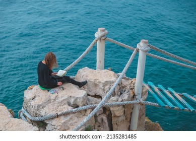 woman sitting at the edge drawing picture seascape suspension bridge