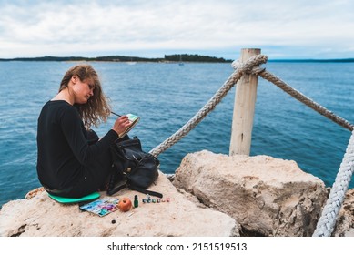 woman sitting at the edge drawing picture seascape suspension bridge