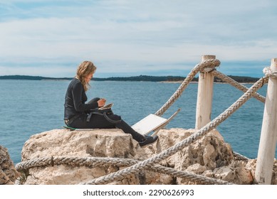 woman sitting at the edge drawing picture seascape
