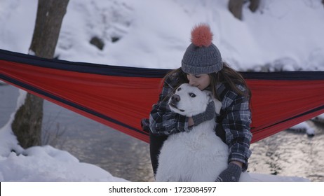 Woman Sitting In Hammock Holding And Petting Her Dog As Dog As Look On It Face Wanting To Get Away In Winter.