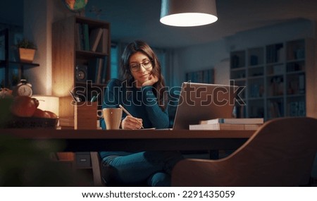 Woman sitting at her desk and connecting with her laptop late at night, she is studying and attending online classes